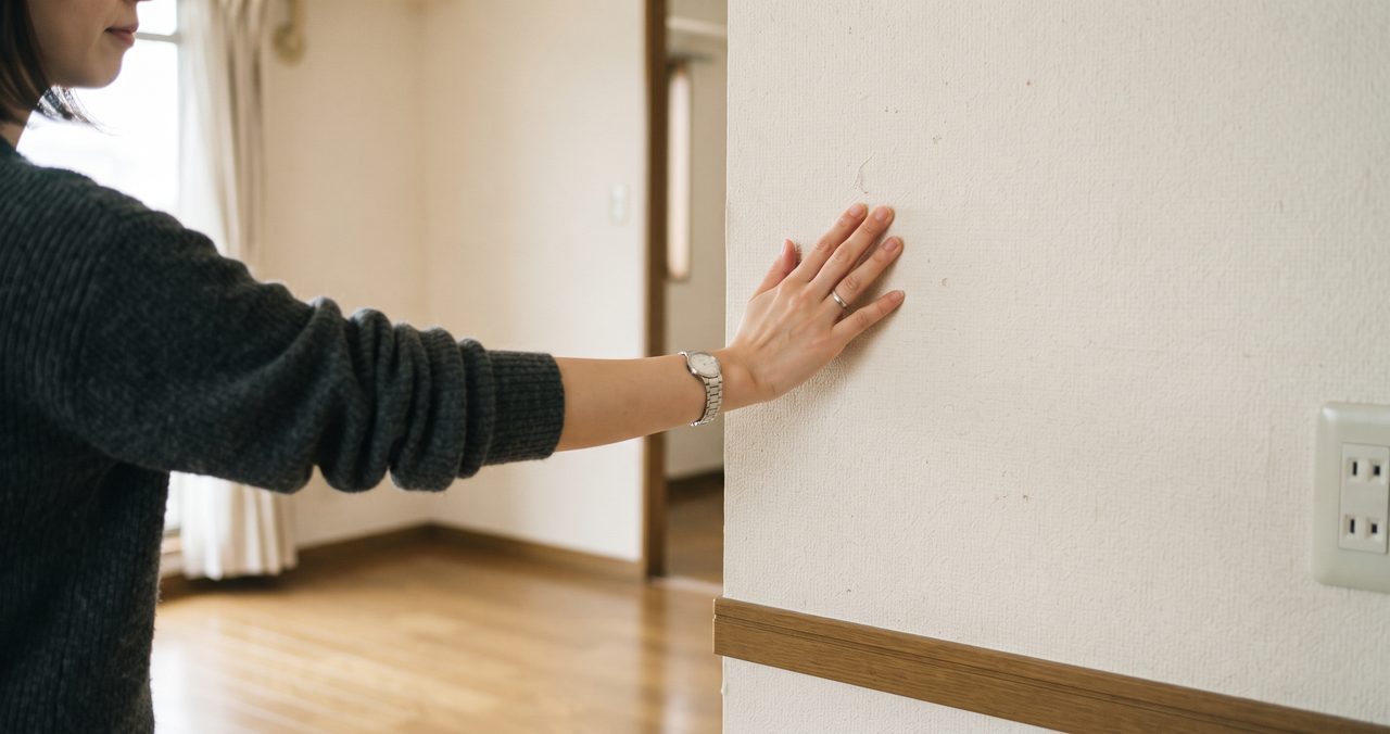 内見中に賃貸マンションの壁を手のひらでそっと叩いて、音の響き方を確認している人の手元のクローズアップ